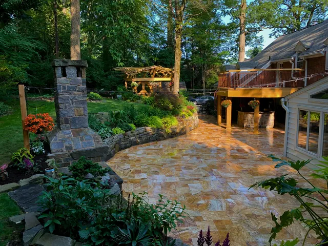 Flagstone patio with a stone chimney, curved stone wall and planted beds
