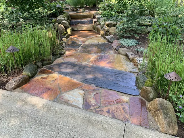 Flagstone walkway and steps edged with boulders, ornamental grasses and path lights