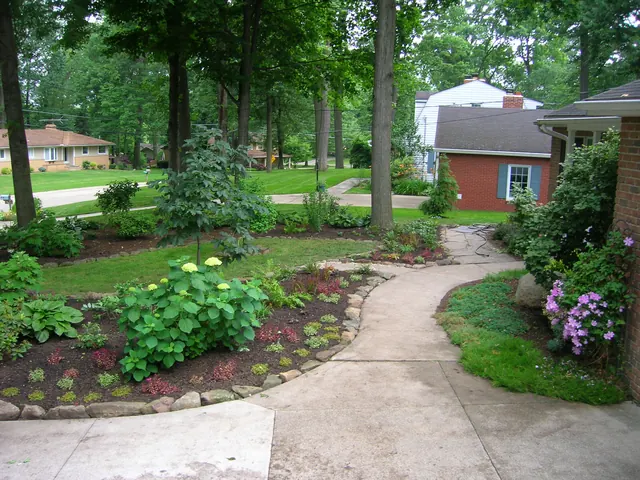 Curved front walkway lined with stone-edged beds of hydrangeas and shrubs
